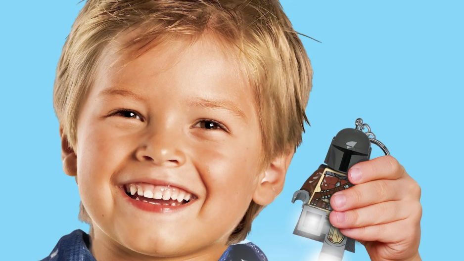 Imagem de um menino branco loiro sorrindo segurando um brinquedo lego do Mandalorian
